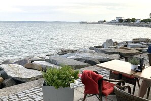 Een restaurant aan zee met terras, uitzicht op de zee en een rotsachtige kustlijn.