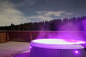 Un jacuzzi en una terraza de madera con un bosque de fondo.