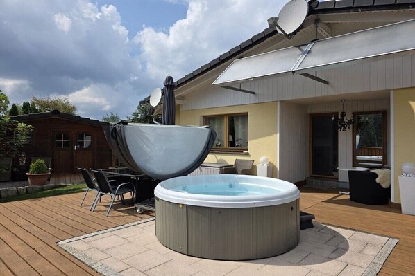 Un jacuzzi en una terraza de madera con una casa al fondo.