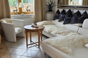 A modern living room with a white sofa, a round wooden coffee table, and a white furry throw. - Holiday home with 2 bedrooms (Lenzkirch)