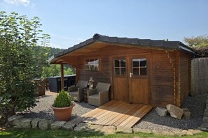 Una cabaña de madera con un porche, una pequeña zona de estar y una planta en maceta.