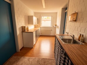 A narrow kitchen with white brick walls, a window, a radiator, and a wooden countertop with a sink. - Vrbo Property (Aidlingen)