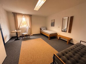 A bedroom with a bed, a bench, a chair, a small table, a mirror, and a window with curtains. - Vrbo Property (Aidlingen)