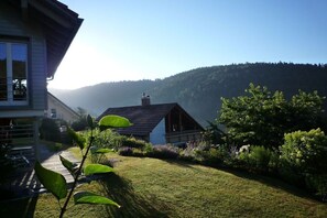 Une maison avec un toit en pente, entourée d’une pelouse bien entretenue et de diverses plantes.
