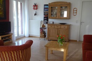 A living room with a television, a wooden cabinet, and a table with flowers. - Carla Family van der Meyden (Todtmoos)