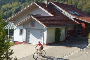 A cyclist riding a bicycle in front of a building with a sloped roof and a garage. - Carla Family van der Meyden (Todtmoos)