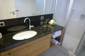 A bathroom with a black countertop, a white sink, a mirror, and a glass-enclosed shower. - Carla Family van der Meyden (Todtmoos)