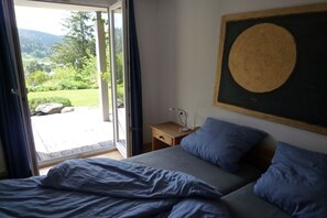 A bedroom with a bed, a nightstand, a painting, and a view of a garden through a sliding door. - Carla Family van der Meyden (Todtmoos)