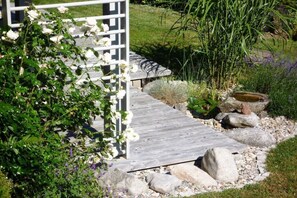 Een houten pad dat leidt naar een witte pergola met klimrozen.