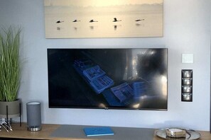 A flat-screen TV mounted on a wall, a potted plant, a lamp, and a framed picture above the TV.