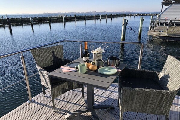 Une terrasse avec une table dressée pour deux personnes, donnant sur une étendue d’eau calme.