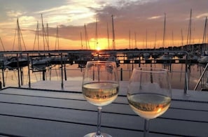 Dos copas de vino blanco sobre una mesa, con un puerto deportivo y barcos al fondo.