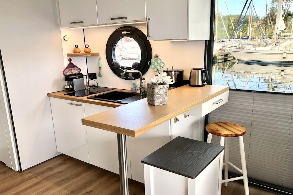 Eine moderne Küche mit einer Holz Arbeitsplatte, einem runden Fenster und Blick auf Boote.