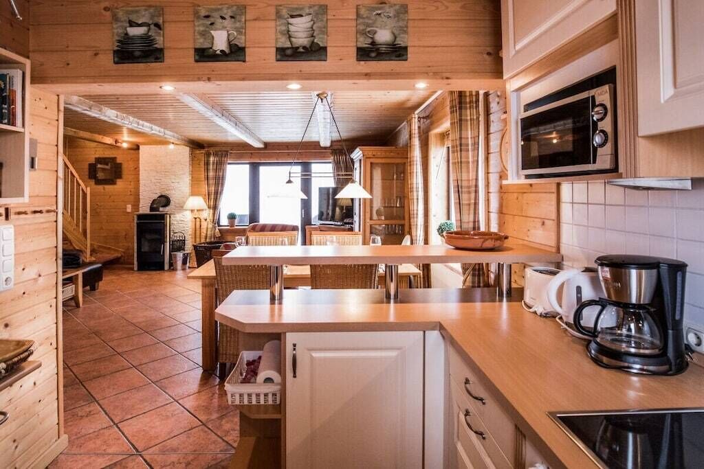 A wooden interior with a kitchen area, including a microwave, coffee maker, and a dining table with chairs.