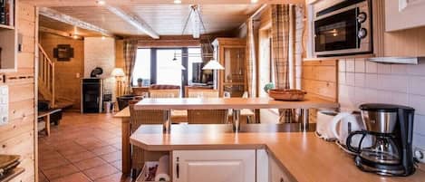 A wooden interior with a kitchen area, including a microwave, coffee maker, and a dining table with chairs.