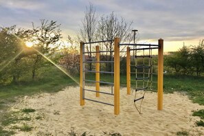 A playground with a climbing structure and a slide, set on sandy ground with trees in the background. - Holiday home in the Harz Mountains with 2 bedrooms (Hasselfelde)