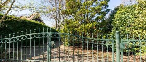 A gated entrance with a metal fence, a pathway leading to a building, and surrounding greenery.