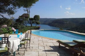 An infinity pool with a view of a lake and hills, outdoor seating, and a table with chairs. - Holiday home with 3 bedrooms (Esparron de Verdon)