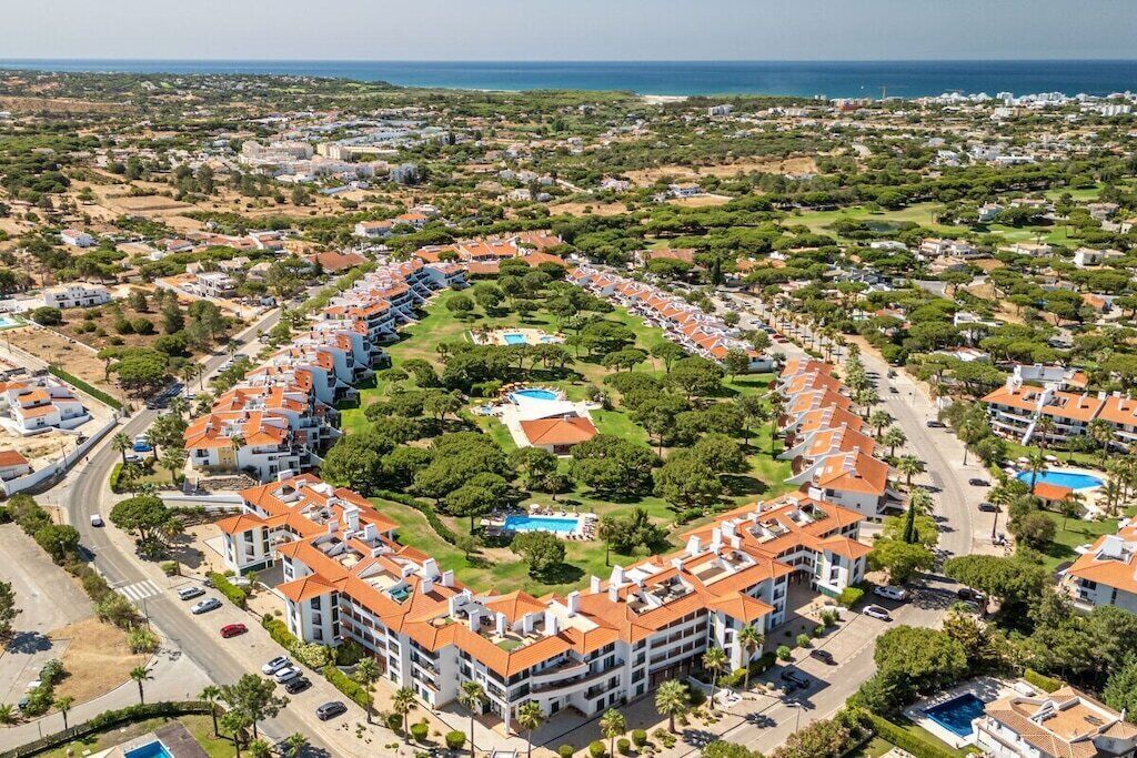 A residential area with a circular layout of buildings, a central green space with a pool, and a view of the sea.