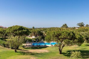 Ein Poolbereich mit Liegestühlen und Sonnenschirmen, umgeben von Bäumen und blauem Himmel.
