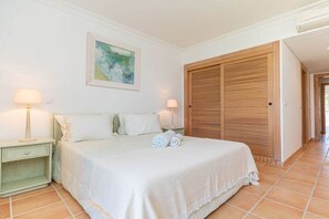 Un dormitorio con una cama, dos mesitas de noche, un armario de madera y un cuadro en la pared.