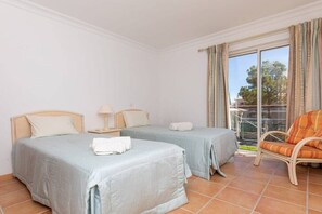 Ein Hotelzimmer mit zwei Betten, einem Sessel und einem Balkon mit Vorhängen.