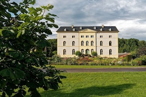 A large, symmetrical building with multiple windows and a central entrance, surrounded by a well-maintained garden.