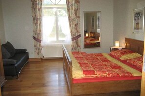 Une chambre à coucher avec un lit en bois, un canapé noir, une fenêtre avec des rideaux et un miroir sur le mur.