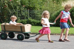 Two children walking on a paved path with a wooden cart.