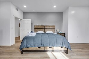 Een slaapkamer met een bed, houten hoofdbord, nachtkastjes en een deur.