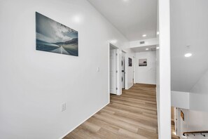 A hallway with a wooden floor, white walls, and a painting of a landscape. There are doors leading to other rooms. - Stylish Townhome w/ 4 King Beds, Walk to ASU (Tempe)