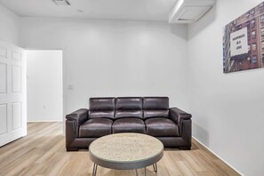 A room with a brown leather sofa, a glass coffee table, and a white wall with a framed picture. - Stylish Townhome w/ 4 King Beds, Walk to ASU (Tempe)