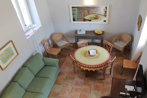 Une pièce avec un canapé vert, une table de salle à manger ronde entourée de chaises, un petit meuble et un tableau encadré accroché au mur.