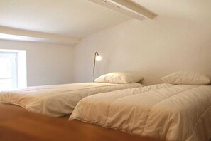Ein Zimmer mit zwei Betten, einer Nachttischlampe und einem Fenster.