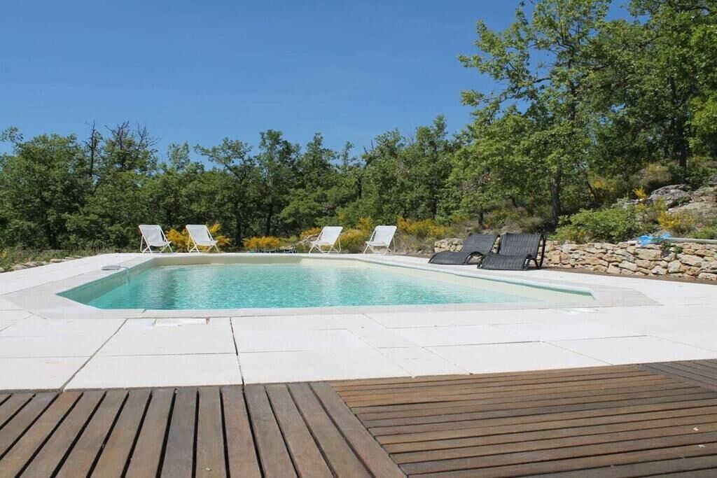 A rectangular swimming pool with a wooden deck in the foreground and lounge chairs around the pool.