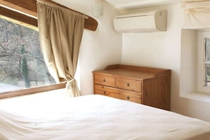 Une chambre à coucher comprenant un lit, une commode en bois, un appareil de climatisation et une fenêtre avec des rideaux.