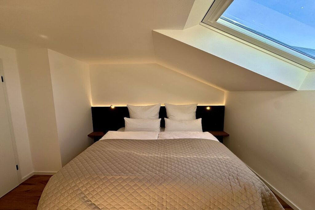 A bedroom with a sloped ceiling and a skylight, a bed with a quilted cover, and bedside lamps.
