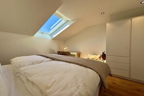 Ein Schlafzimmer mit Dachfenster, einem Bett, einem Schreibtisch und einem Kleiderschrank.