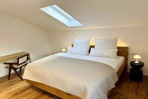 A bedroom with a skylight, a bed with white bedding, a bedside table with a lamp, and a wooden desk. - Holiday apartment with 1 bedroom (Wertach)