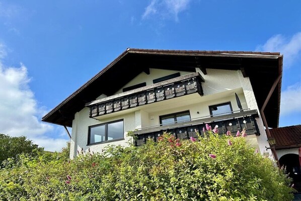 A two-story building with a balcony, surrounded by greenery. - Holiday apartment with 1 bedroom (Wertach)