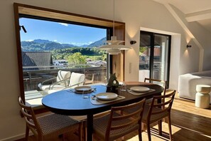 A dining area with a table set for two, a view of a mountain landscape, and a balcony with a railing. - Holiday apartment with 1 bedroom (Wertach)