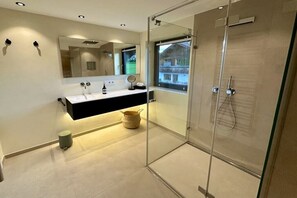 A modern bathroom with a glass-enclosed shower, a large mirror, and a window providing a view of the outside. - Holiday apartment with 1 bedroom (Wertach)