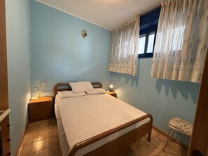 A bedroom with a single bed, bedside lamps, a nightstand, and a window with curtains. - Practical beachside flat for four travellers (Bibione)
