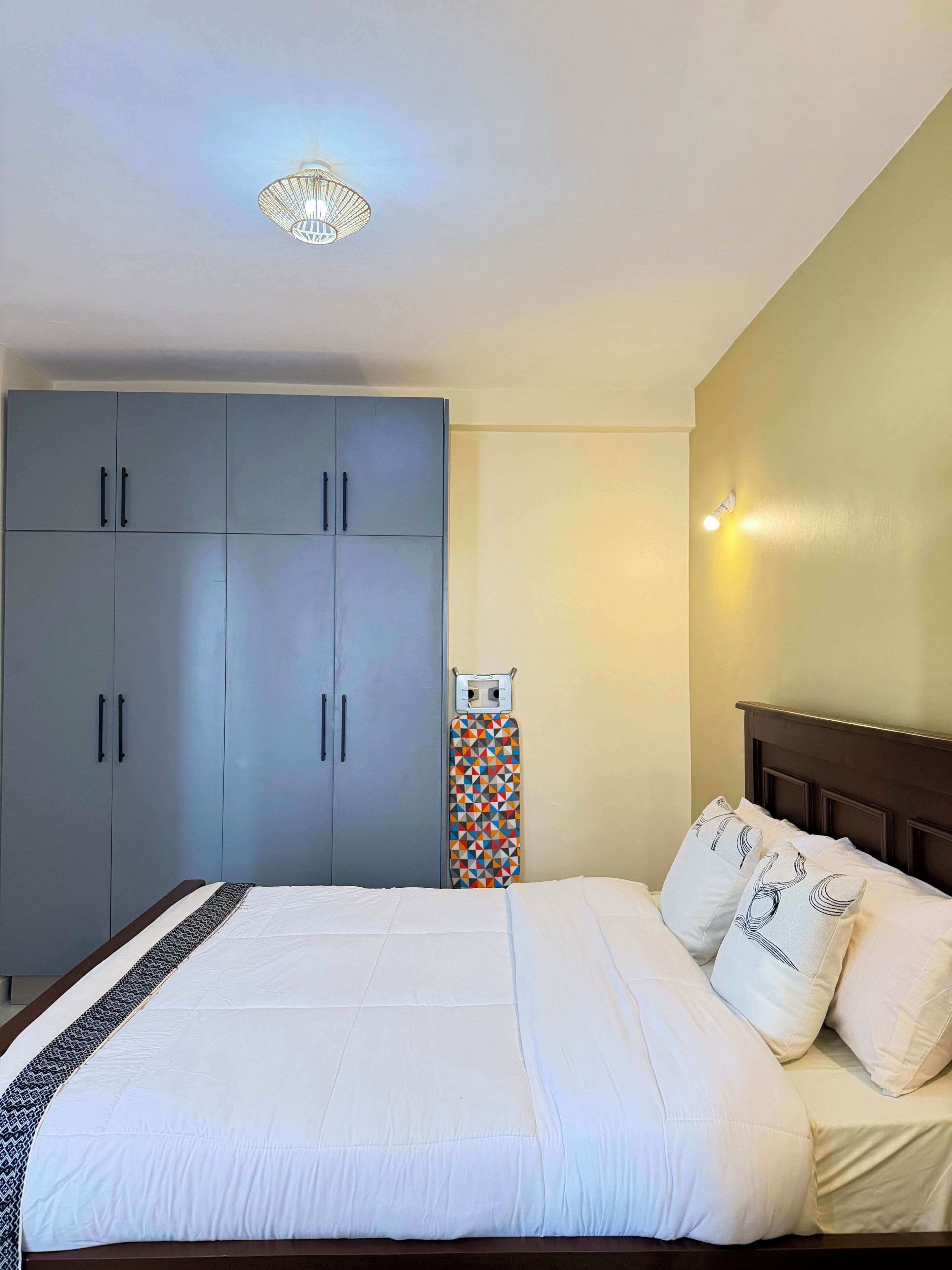 Une chambre à coucher comprenant un lit, une armoire et une planche à repasser fixée au mur.