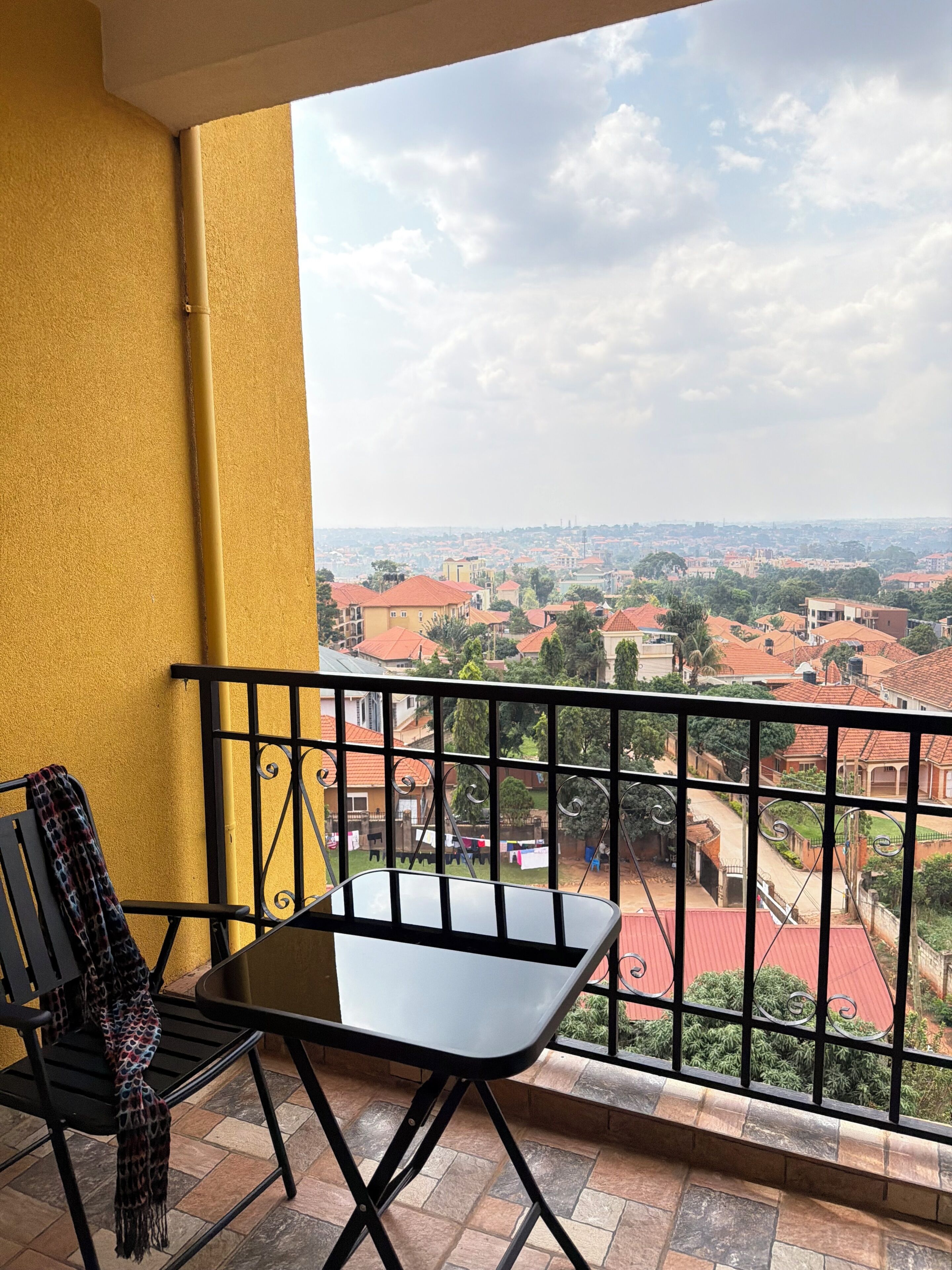Un balcon avec une table et des chaises, donnant sur un quartier résidentiel avec des maisons aux toits rouges.