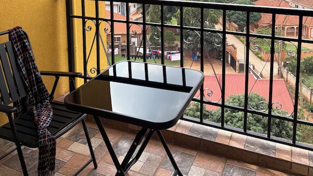 Ein Balkon mit Tisch und Stühlen, mit Blick auf eine Wohngegend mit Häusern mit roten Dächern.
