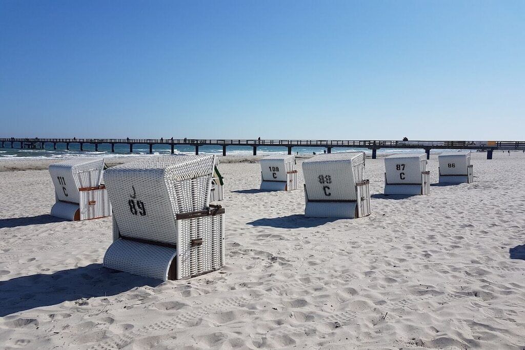 Beach chairs labeled with numbers on a sandy beach with a pier in the background.