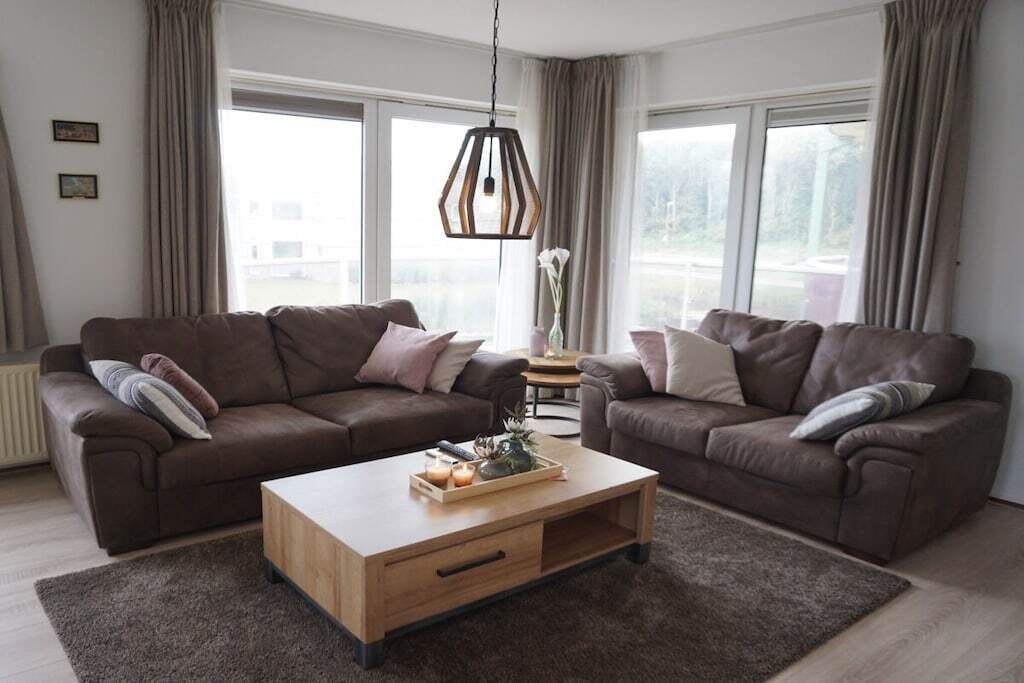 Una sala de estar moderna con dos sofás, una mesa de centro de madera y una lámpara colgante.