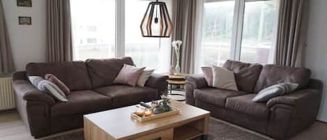A modern living room with two sofas, a wooden coffee table, and a hanging light fixture.