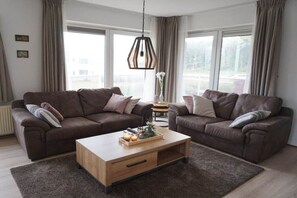 Een moderne woonkamer met twee banken, een houten salontafel en een hanglamp.